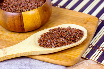 Brown raw dry flax seeds in a wooden spoon on a light textile background.