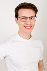 Portrait of a cute guy with glasses and a white T-shirt on a white background who smiles and gullible right into the camera.