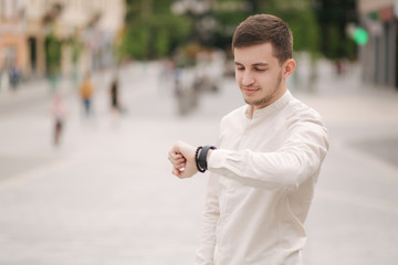 Man looking at the watch outdoors. Young man in white shirt in the city