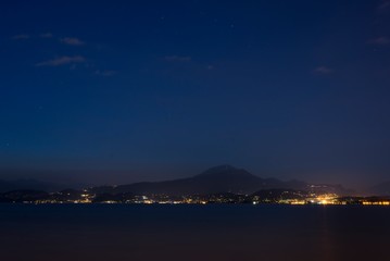 Night shot from a coast of Peschiera del Garda to the Garda lake and mountains with lights all over the other coast. Lights of Garda town in the night from other coast.
