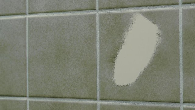 Cleaning bathroom tile with sponge and cleaning product