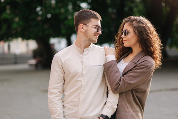 Fototapeta premium Happy couple walking in the city. Attractive young woman with curly hair and handsome young man in centre of the city. Smiled people in sunglasses outdoors