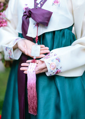 Hands of a Korean woman dressed in a white national green hanbok costume holding a traditional accessory - norigae pendant with a carved image on the stone