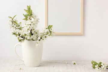 blooming plum branches with white flowers in a Cup and an empty wooden frame.