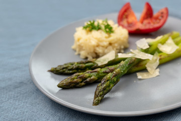 Green asparagus served with parmesan, rice and tomato on a plate on a gray blue tablecloth, copy space, close-up shot