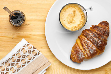 Top view on a breakfast consisting of a cup of coffee, a croissant with jam on a wooden table with copy space