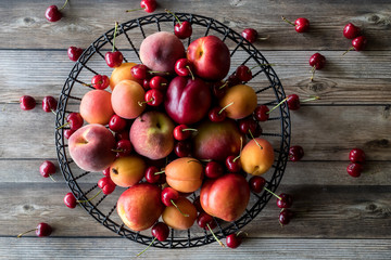 Horizontal view of a metal bowl filled with stone fruit against a wooden table.