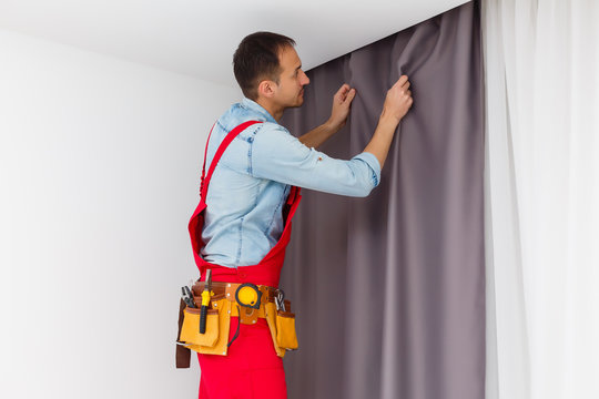 Handy man home Installation and repair service technician or home owner hanging curtains for the window treatment in a new house.