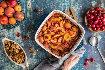 A top down view of a casserole dish of delicious baked stone fruit cobbler with a hand and napkin holding one end.