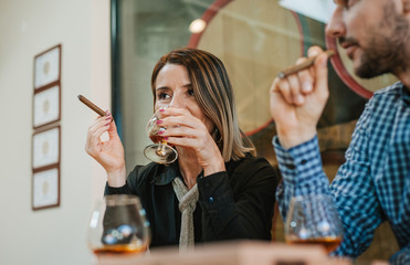 Portrait of a woman drinking brandy and smoking Cuban cigarettes in a restaurant, a man with a cigarette sitting next to her