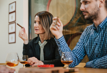 Portrait of a woman drinking brandy and smoking Cuban cigarettes in a restaurant, a man with a cigarette sitting next to her
