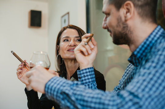 A man and a woman toast in a restaurant with brandy while smoking tompus