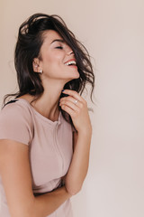 Joyful tanned woman posing in T-shirt against beige background. Photo of cute lady with sincere smile