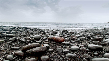 Beautiful landscape of wet pebbles and rocks lying on ocean shore at cloudy day