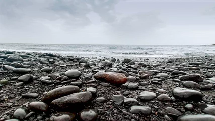 Fototapete Schwarz Schöne Landschaft aus nassen Kieselsteinen und Felsen, die an bewölkten Tagen am Meeresufer liegen