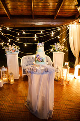 night wedding ceremony, the arch is decorated with flowers, candles and garlands of light bulbs and there is a wedding cake on the table