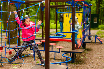 Fototapeta na wymiar happy little girl in a rope park on the wood background