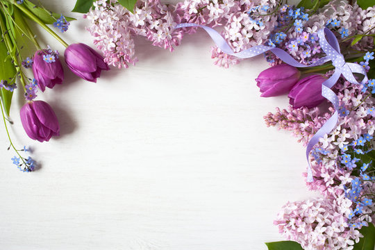 Pink lilac flowers, purple tulips and forget-me-nots on a wooden background. Space for congratulations text.