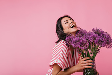Girl in pink sundress enjoys scent of flowers and sincerely laughs, enjoying great spring day on...