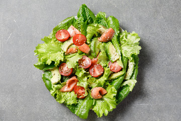 Salmon salad with avocado, green leaves, tomatoes on gray background