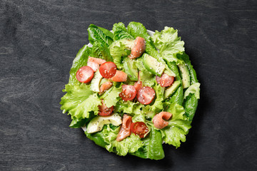 Salmon salad with avocado, green leaves tomatoes on dark background.