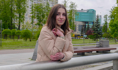 Cute smiling girl is standing on the promenade in the background of a city park