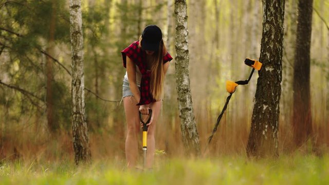 Young woman digging the treasure discovered with metal detector in the forest.