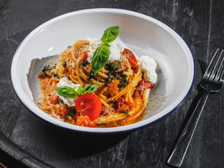 Pasta spaghetti with basil and cheese on black barrel