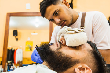 Obraz na płótnie Canvas Young Latin Barber At Work In Stylish Barbershop. Cool, bearded man enjoys the moment.