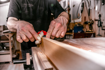 a male carpenter working in atelier, planing a wood piece with a double hand push woodworking bird planer, closeup. 