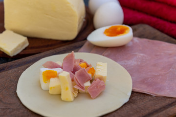 Empanada de jamón y quesos, sus ingredientes,   primer plano sobre una tabla de madera rústica