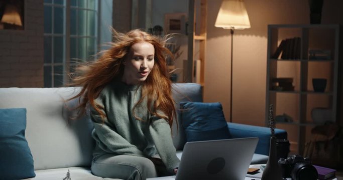 Pretty caucasian redhead girl looking at laptop screen, hair blowing, reading breaking news, seeing shocking discount during online shopping, vowing in amazement 4k footage