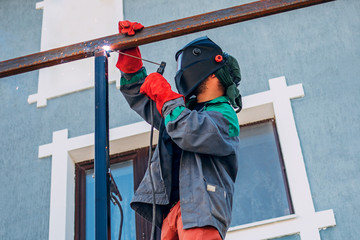 A welder welds a metal pole with electric welding, holds an electrode in his hands