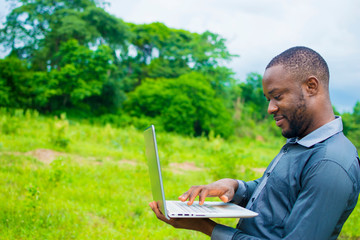 young handsome black african business man standing on a farmland using his laptop.