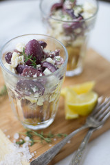 Feta and black olive appetizer with lemon and thyme in a glass on wood surface