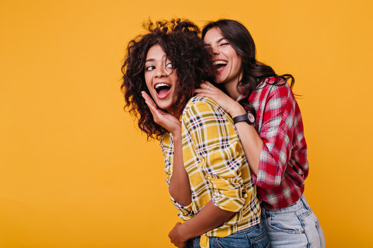 Surprised Mulatto Covers Her Mouth From Unexpected Meeting With Her Best Friend. Lady In Red Shirt With Black Watch On Her Hands Scared Girl From Back And Laughs