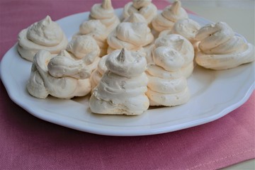 French white irregular shaped meringue on a round glossy plate, against a background of pink linen.