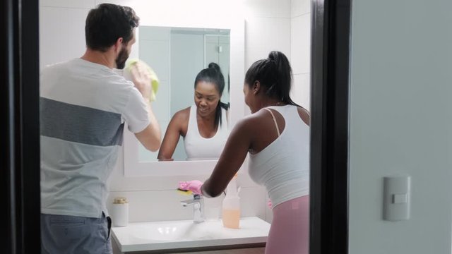 Interracial couple doing chores and cleaning bathroom at home. African American wife helping Caucasian husband with soap, detergent and sanitizer in toilet. Domestic task with happy married people