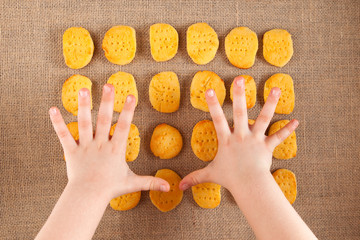 The child's hands reach for gluten-free cookies. Homemade biscuit lie on burlap. Rustic style
