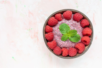 Chia seed pudding with almond milk, yogurt and pitaya dragon fruit powder, raspberries and peppermint leaves in coconut bowl. Superfood and vegan food concept. Pink background, copy space