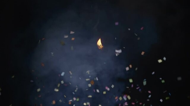 New Year's cracker exploded powerfully and a cloud of confetti fly away in smoke on black background. Slow motion. High speed camera