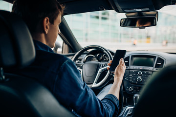man sitting behind the wheel of a car, using a mobile phone while driving a car