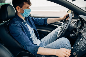 A man in a protective medical mask, sitting behind the wheel of a car. Quarantine, coronavirus