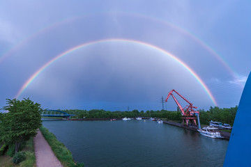 Fototapeta na wymiar Double beautiful rainbow after rain in the sky above the river and the old crane