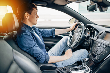 A handsome young man in a denim shirt sitting in a car at the wheel