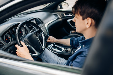 man who buys a car while sitting in the driver's seat is testing the car at a car dealership.