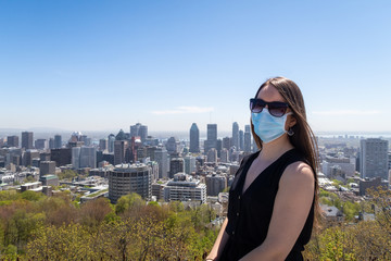 Young woman wearing a chirurgical mask at the Kondiaronk belvedere, with Montreal's city skyline in the background