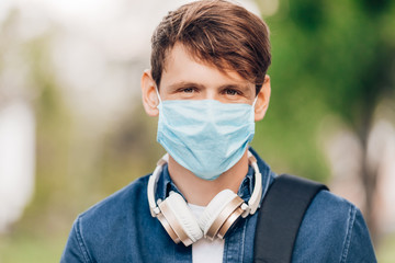 man in a protective medical mask on his face walks through the Park with wireless headphones around his neck. Quarantine, coronavirus