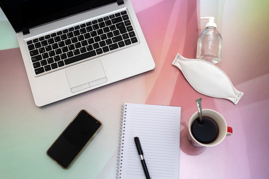 computadora sobre mesa con anotador lapicera una taza de cafe celular con barbijo y alcohol en gel para proteccion del covid-19 trabajo en casa 