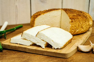 Sliced ​​cheese with garlic and herbs on a wooden board closeup